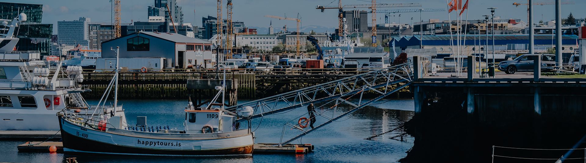 Workboat tied up at a busy commercial harbor with cranes behind